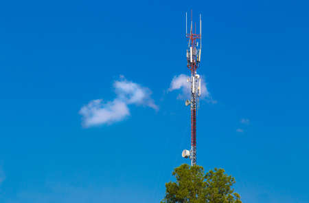 skinny tall telecommunication tower against deep blue sky and white fluffy clouds with foreground...