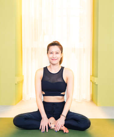 young attractive happy asian woman in black yoga exercise outfit sitting and smiling at home, bathed...