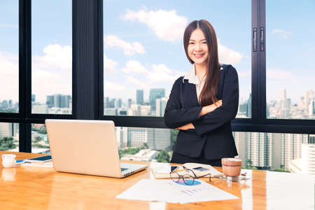 happy attractive businesswoman in suit standing behind her desk, with computer, other working...