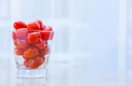 small red cherry tomatoes in wet clear glass cup on white table with blur background, concept for healthy diet, eating fruit and vegetable, heathy food, space for text, or copy spaceの写真素材