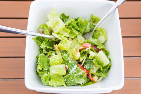 healthy food, caesar salad in a white bowl with fork and spoon on wooden table, good for health articleのeditorial素材