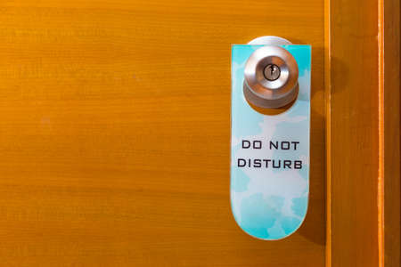 old Do Not Disturb sign tag haning on metal door knob, concept of needing privacy, room for text or copyspaceの写真素材