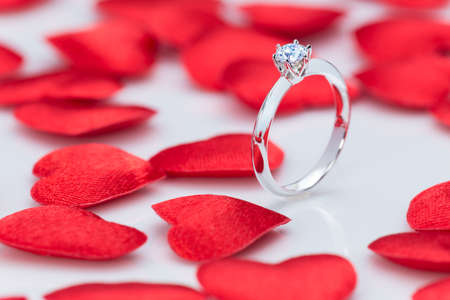 beautiful diamond ring on white table with small red felt hearts, good concept for love, wedding or special occasionの写真素材