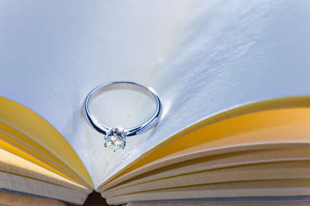 beautiful diamond ring on blank open book with cool and warm color tone, room for copy space, good concept for wedding, engagement, or special occasionsの写真素材