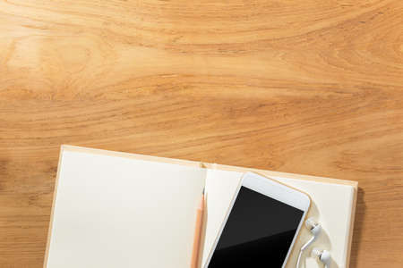 planning concept with cellphone, earphone, pencil and open blank paper notebook on wooden table, room for text or copy spaceの写真素材