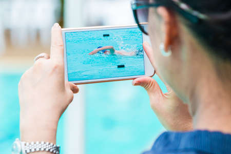 woman taking picture of her son swimming with her smart phone, selective focus on the phone's screen, good for sport or technology conceptの写真素材