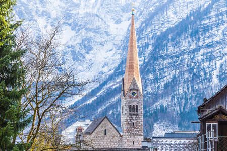 view of one of the Hallstatt's landmarks, the church clock tower standing against mountain background on an early spring day, good for tourism or travel theme backgroundの写真素材