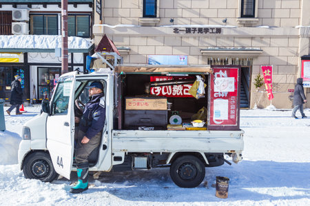 Otaru, Hokkaido, Japan - 30 December 2017 : Baked sweet potato food vendor man waits patiently at his converted grilled mini truck for customers to buy his baked sweet potatoes in Otaru, Hokkaido, Japan on a cold winter day of December 30, 2017のeditorial素材