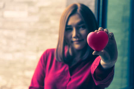 Young happy asian woman holding out pink soft rubber heart to her love one, good for love or valentine concept or themeの写真素材