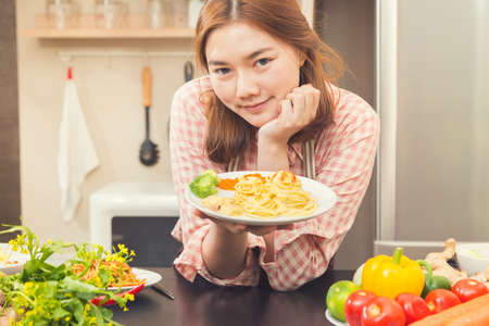 Happy young asian woman proudly holding her cooking result, ham and cheese cabonara spaghetti dish, good for home cooking concept, vintage color toneの写真素材