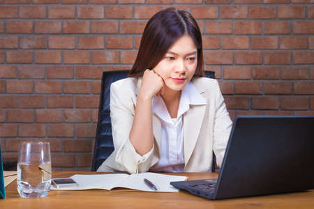 Young asian businesswoman in ligth color suit working late on her laptop computer in her office,...