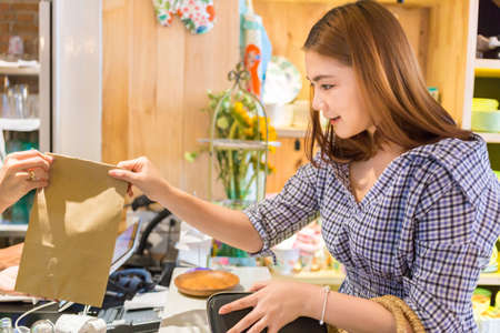 Young attractive Asian woman receiving a bag of goods she has just purchased from the shop seller...