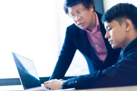 Young Asian businessman working on his computer with his business partner in his office near large...