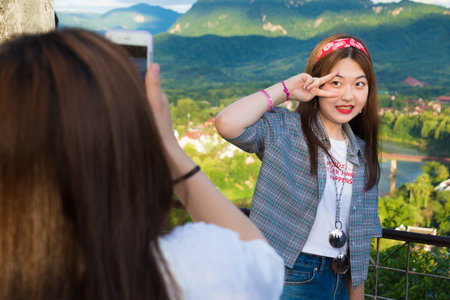 LUANG PRABANG, LAOS - 29 June 2018 - Young Korean tourist takes picture for her friend on top of the Phousi mountain in Luang Prabang, Laos before sunset on June 29, 2018のeditorial素材
