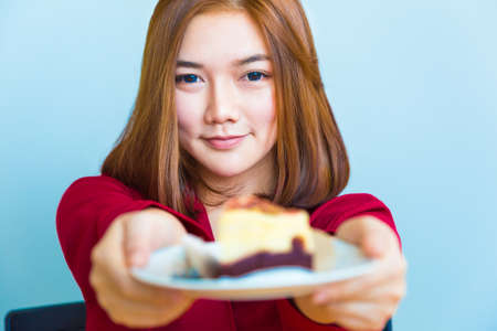 Happy young attractive Asian woman smiling and handing a piece of chocolate cheese cake toward the camera, good for young and happy lifestyle or food conceptの写真素材