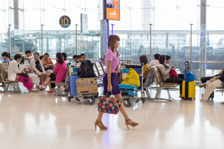 BANGKOK, THAILAND - 21 JULY 2018 - Airline female staff walks by seated Asian tourists inside Suvarnabhumi International AIrport terminal in Bangkok, Thailand on July 21, 2018のeditorial素材