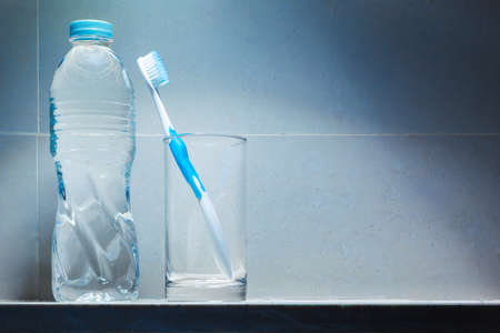 Clean white toothbrush with blue trim in clear drinking glass and a bottle of drinking water on...