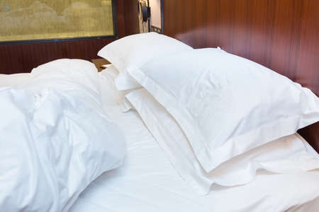 Unmade bed with white sheet and pillows in an old bedroom
