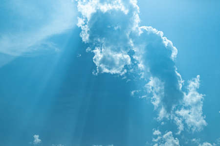Sunny blue sky with soft clouds and bright sun against green trees foreground