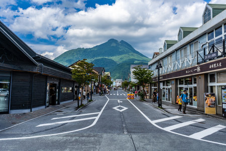 Yufuin, Japan - 12 July 2019 - Tourists walk along the main road from the train station in Yufuin, Japan toward shopping and business area with view of the mountain in background on July 12, 2019のeditorial素材