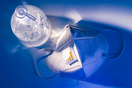 Anti-septic hand gel and N95 mask on white table with dramatic lighting effect, health concept