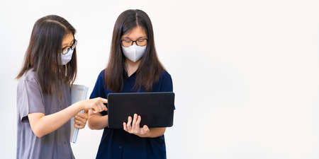 Two young Asian teenagers, wearing masks, working too close together on their school project,...
