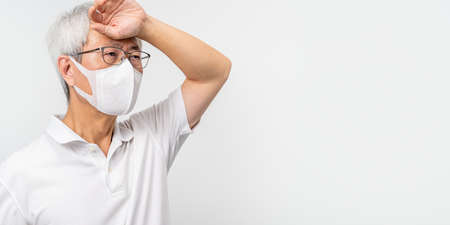 Old Asian man wearing N95 mask, putting his hand on his forehead, feeling sick, white background - COVID-19 virus concept, room for copy spaceの写真素材