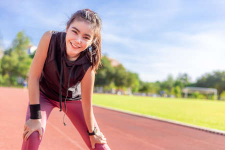 Happy smiling beautiful young Asian woman exercising in the morning at a running track, good healthy lifestyle conceptの写真素材