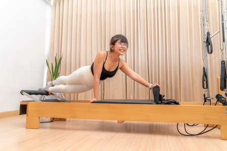 Happy young Asian woman working on pilates reformer machine during her health exercise trainingの写真素材