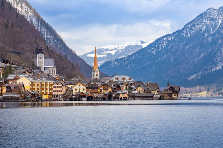 VIew of beautiful Hallstatt lake and famous church during morning sunrise in early spring with mountain ranges covered in some snow in backgrondの写真素材