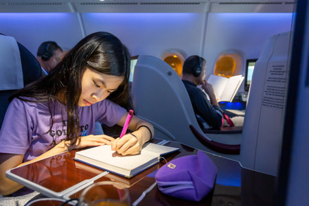 Bangkok, Thailand - 4 April 2015 - An Asian teen write on her notebook while travels on the plane