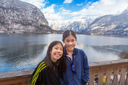 Two happy young Asian sisters post for the photo in front of the Hallstatt lake in Hallstatt,...