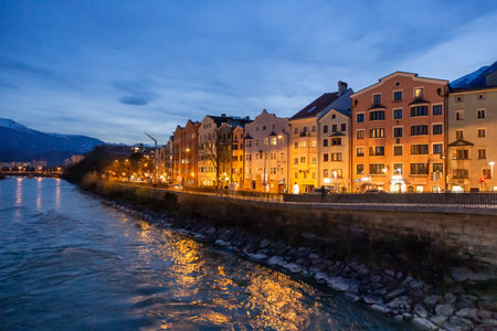 Innsbruck, Austria - 11 April 2015 - Panorama view of colorful buildings and mountains across from the flowing river of Innsbruck, Austria on a late evening night of April 11, 2015のeditorial素材