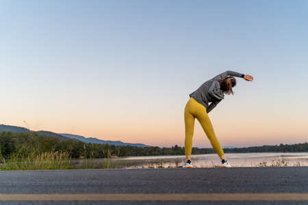 Back view of a woman stretching her arms and legs before her early morning exercise at a local lake...