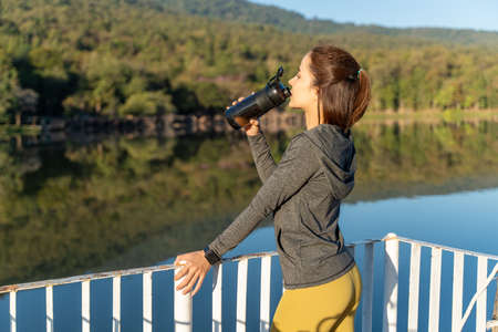 Young attractive and active woman drinking water from her plastic water bottle while taking a break...