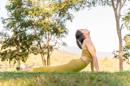 Young attractive and active woman practicing her morning yoga outdoor in her snake pose at a local...
