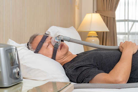 Middle age male with sleep apnea wearing CPAP headgear and mask while sleeping in his bedroom