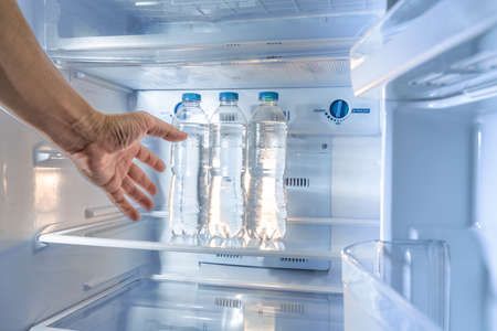 A shaky thirsty male's hand reaching out to grab a cold water bottle from a refrigerator, with motion blur effect added to the handの写真素材