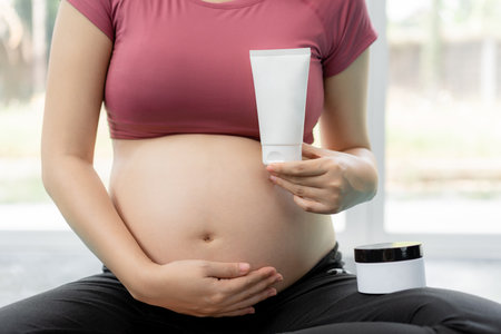 Close up of a pregnant woman in fitness clothes holding a white body gel and cream product to reduce stretch mark during pregnancyの写真素材
