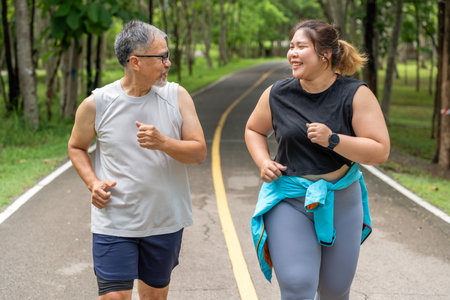 Happy middle age man and young overweight woman enjoy talking to each other during their morning run at a running track of a local parkの写真素材