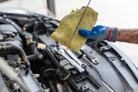 Close up hands of a male car mechanic checking car oil with engine in backgroundの写真素材
