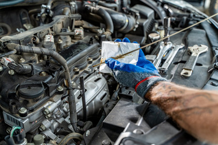 Close up hands of a male car mechanic checking car oil with engine in backgroundの写真素材