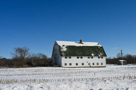 A white barn with many windows against a blue sky and snow covered fields in West Michiganの写真素材