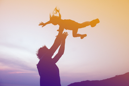 Silhouettes of happy family of father and daughter are having fun on sunset background. Father throws up daughterの写真素材