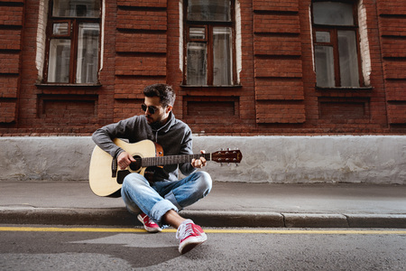 Handsome man is playing on guitar sitting on the roadの写真素材