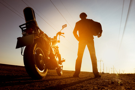 Silhouette of biker with motorbike stands on sunset backdropの写真素材