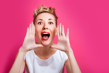 Pretty woman is on the bright pink wall backdrop. She shouts and keeps her arms near face. Looking forwardの写真素材
