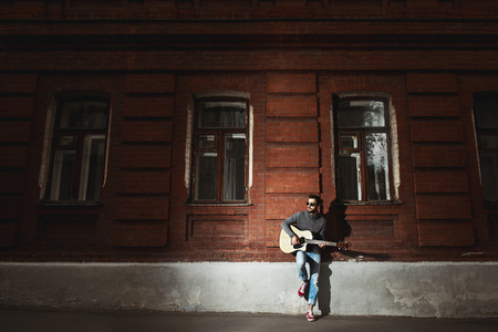 Man stands on brick wall and plays the gitar conceptの写真素材