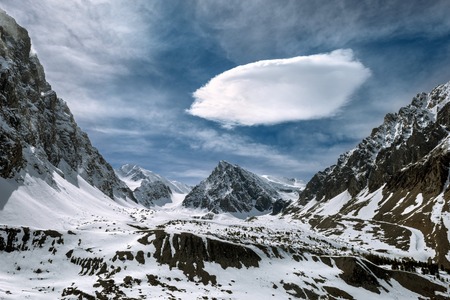 Dark snowy mountains rocks on the cloudy sky backgroundの写真素材