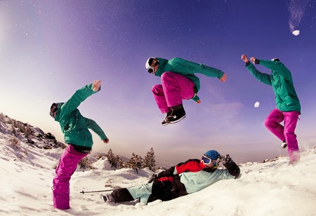 Snowboarder jumps over lying skier on background of snow mountainsの写真素材